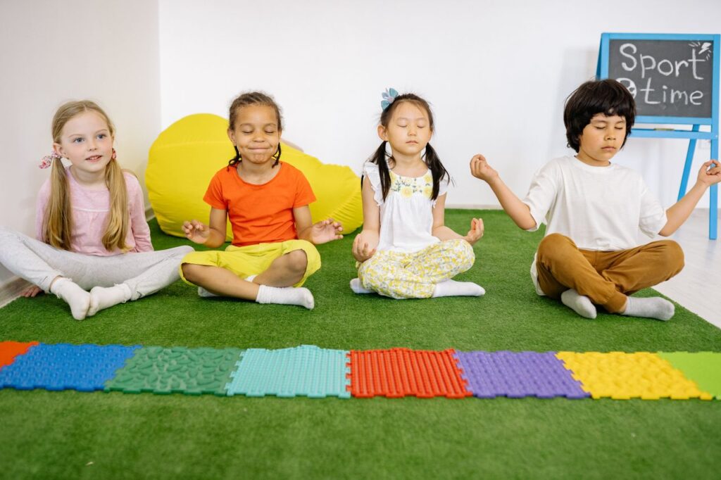 Diverse group of children meditating in a yoga class indoors on artificial grass.